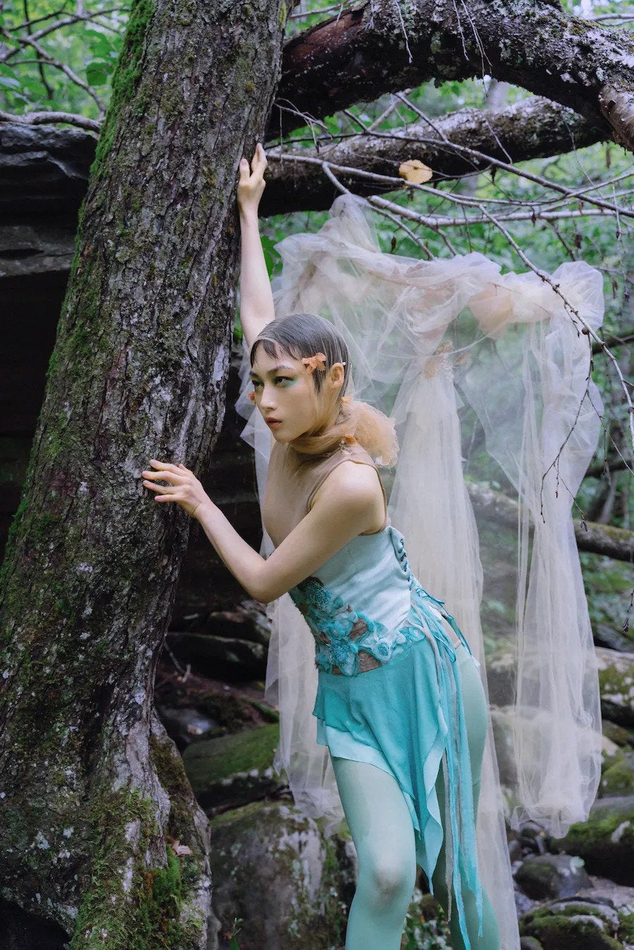 Woman in a forest wearing floral Embroidered lace up corset with shredded silk flowers and embellishments, and a metallic leather lacing