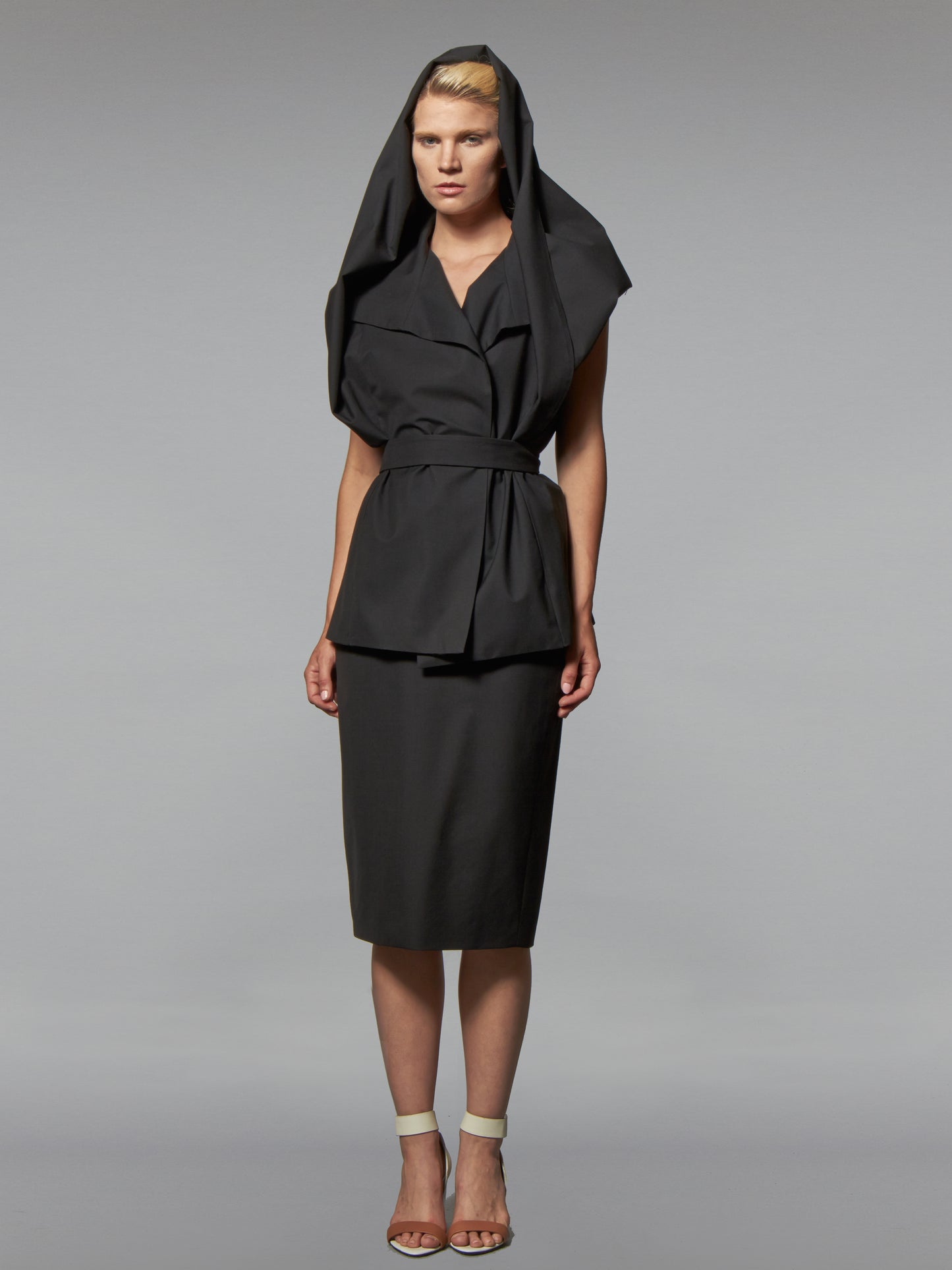 Woman in a black cotton wrap jacket with transformable cape and self tie belt and black skirt