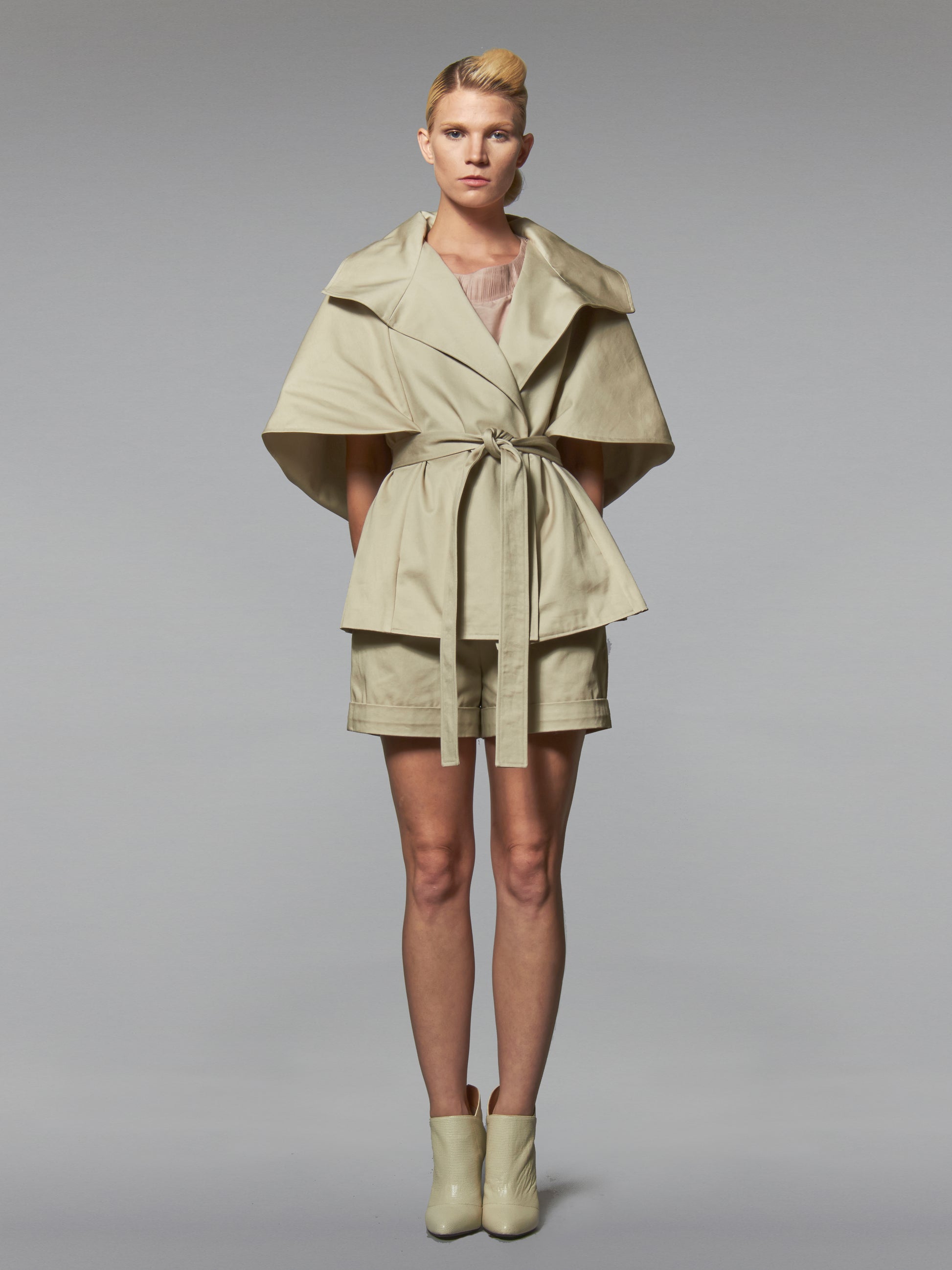 Woman in a beige cotton wrap jacket with transformable cape and self tie belt