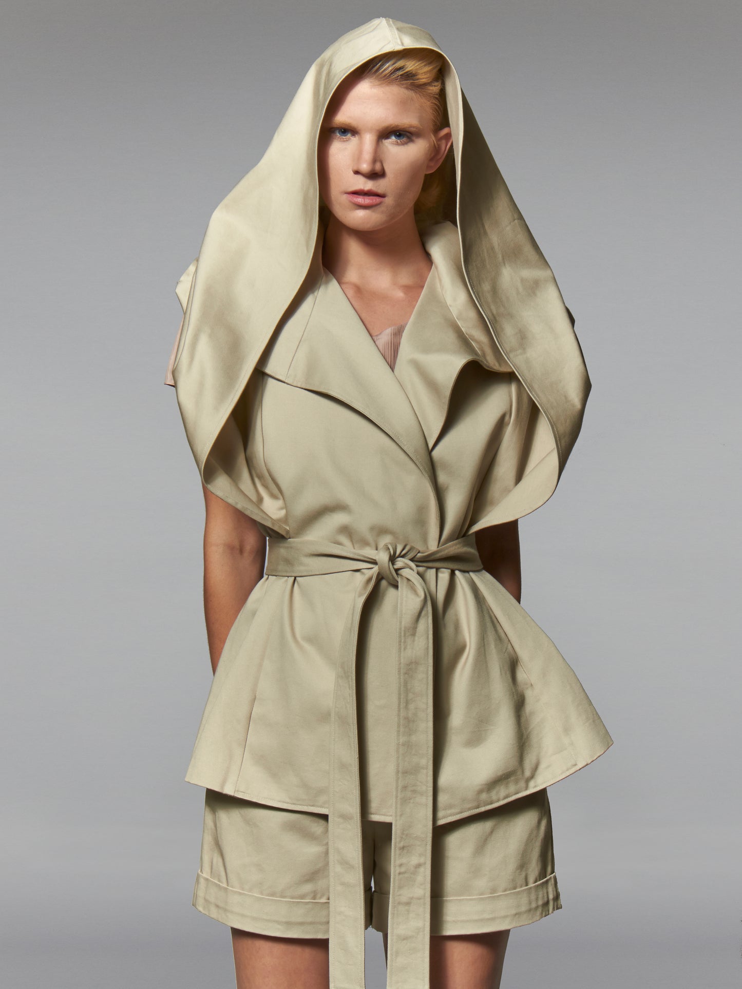 Woman in a beige cotton wrap jacket with transformed hood and self tie belt