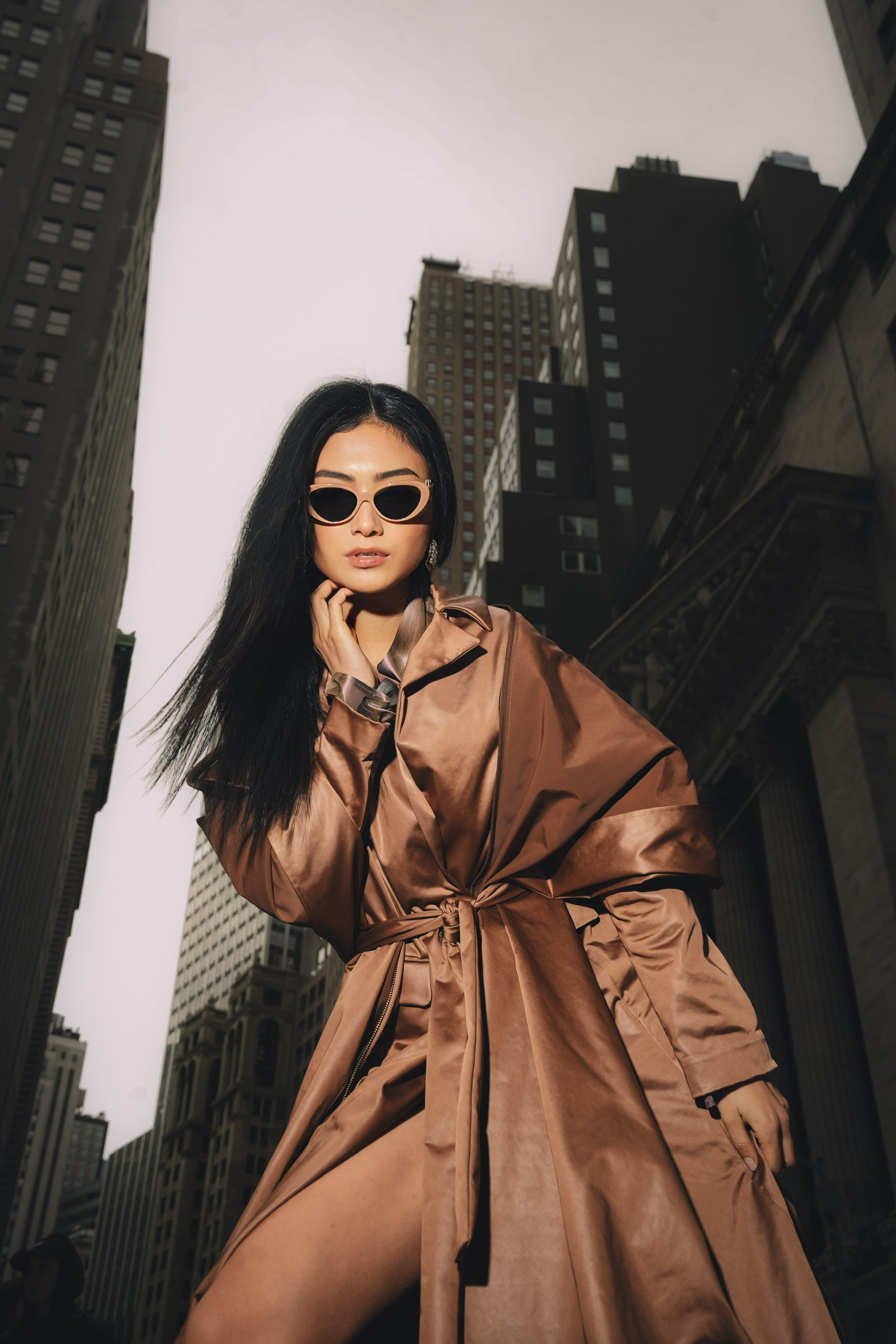 Woman posing wearing sunglasses and copper stretch satin coat with transformable zippers and self tie belt