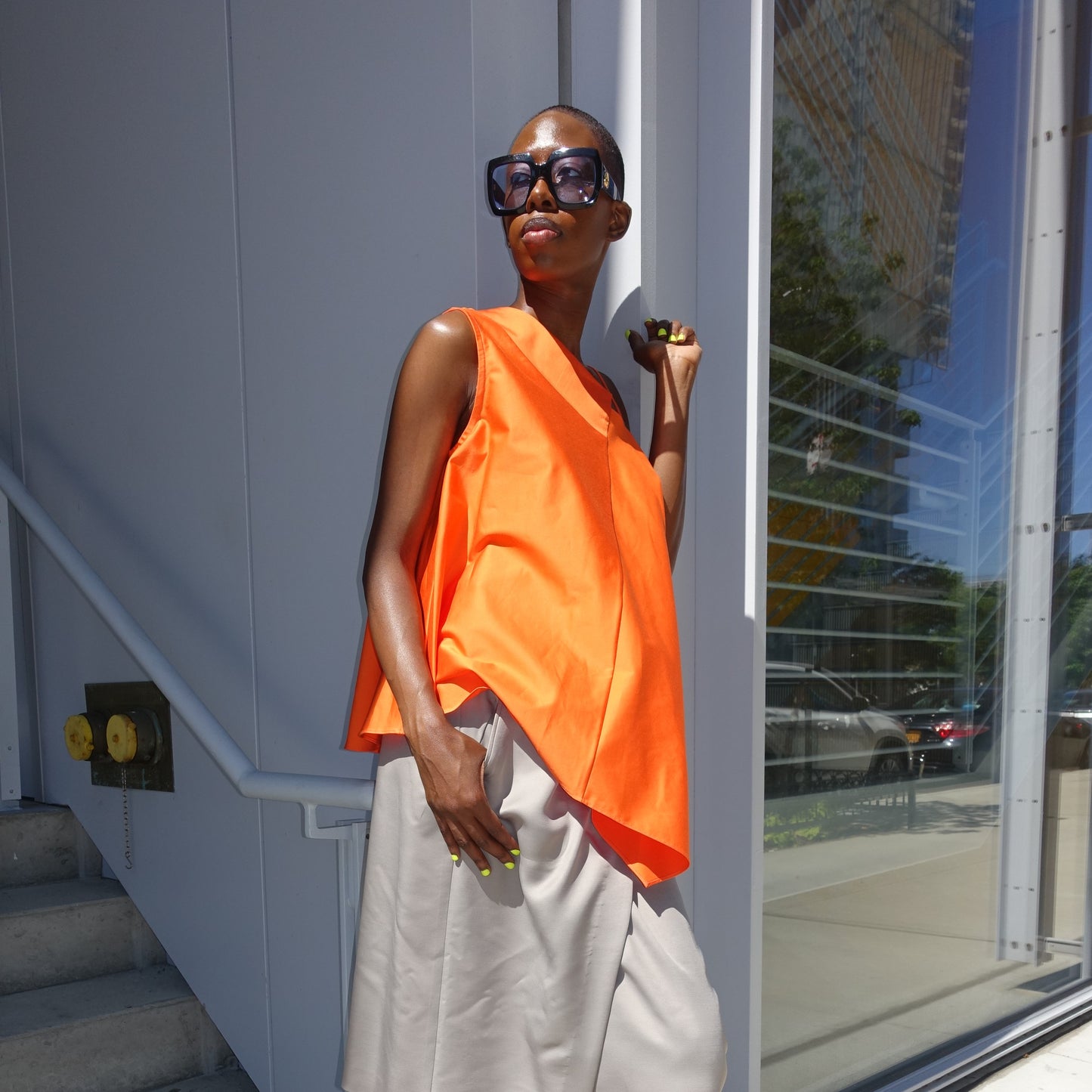 Woman wearing a solid orange one shoulder top with asymmetric shoulder strap