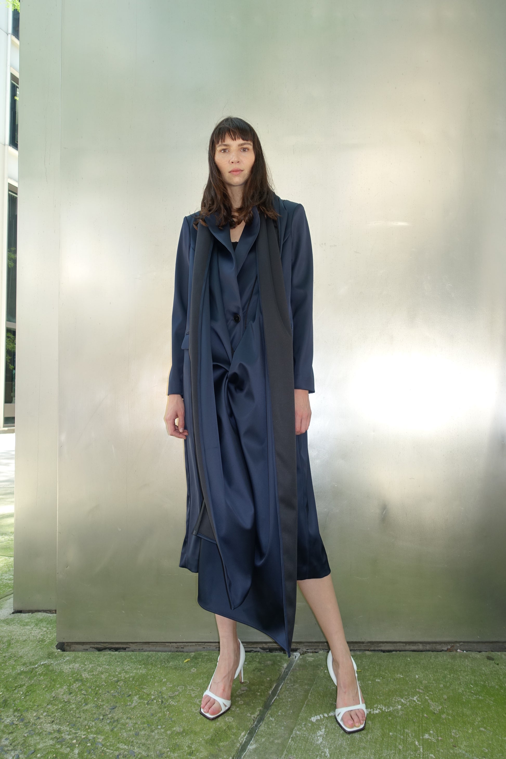 Woman wearing navy navy stretch satin coat with transformable zippers and self tie belt with draped detail over the front