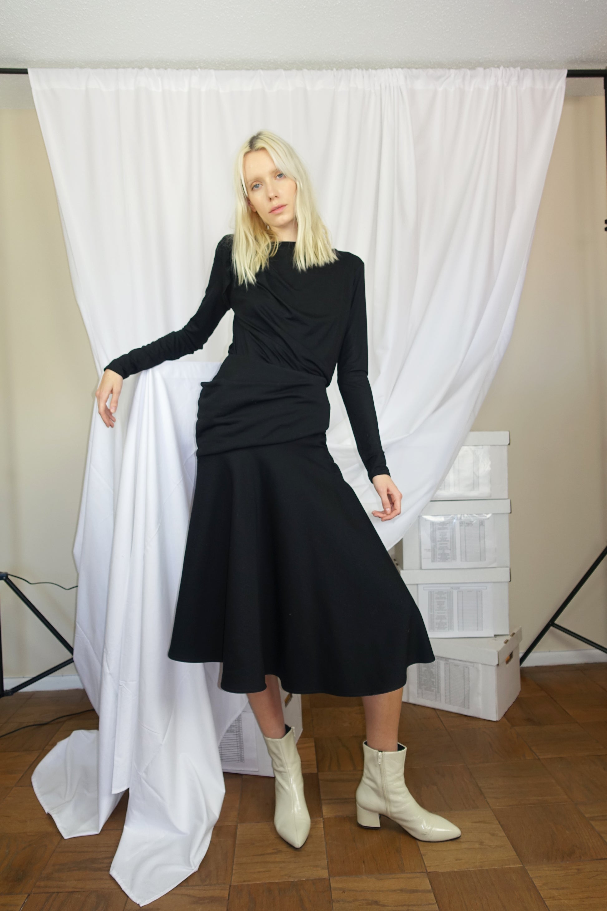 Woman posing in front of curtains wearing a black long sleeve shirt with a black accentuating skirt with stylized cut made of cotton and lyocell