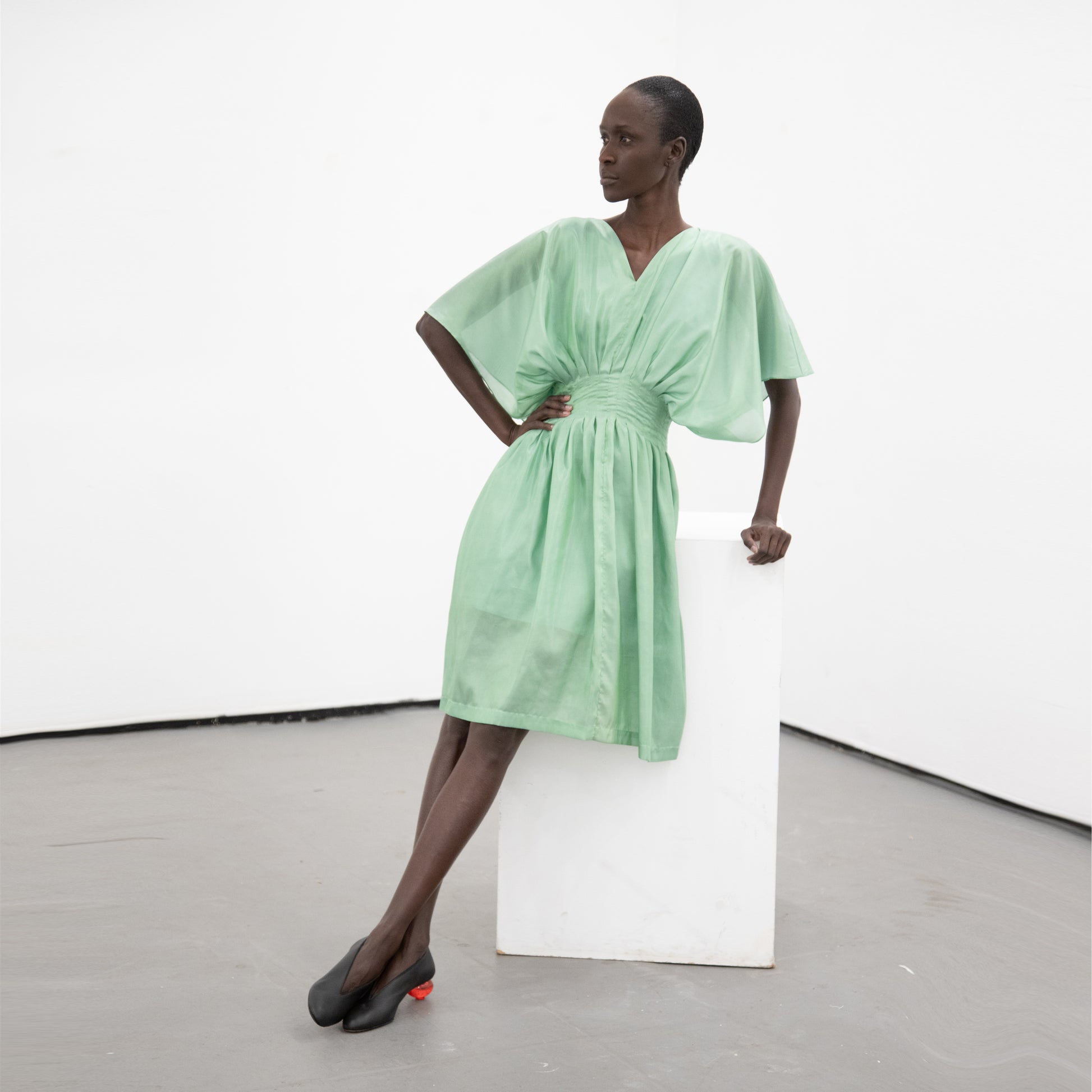 Woman wearing a green loose fitted v neck dress with an integrated corset waist and black shoes