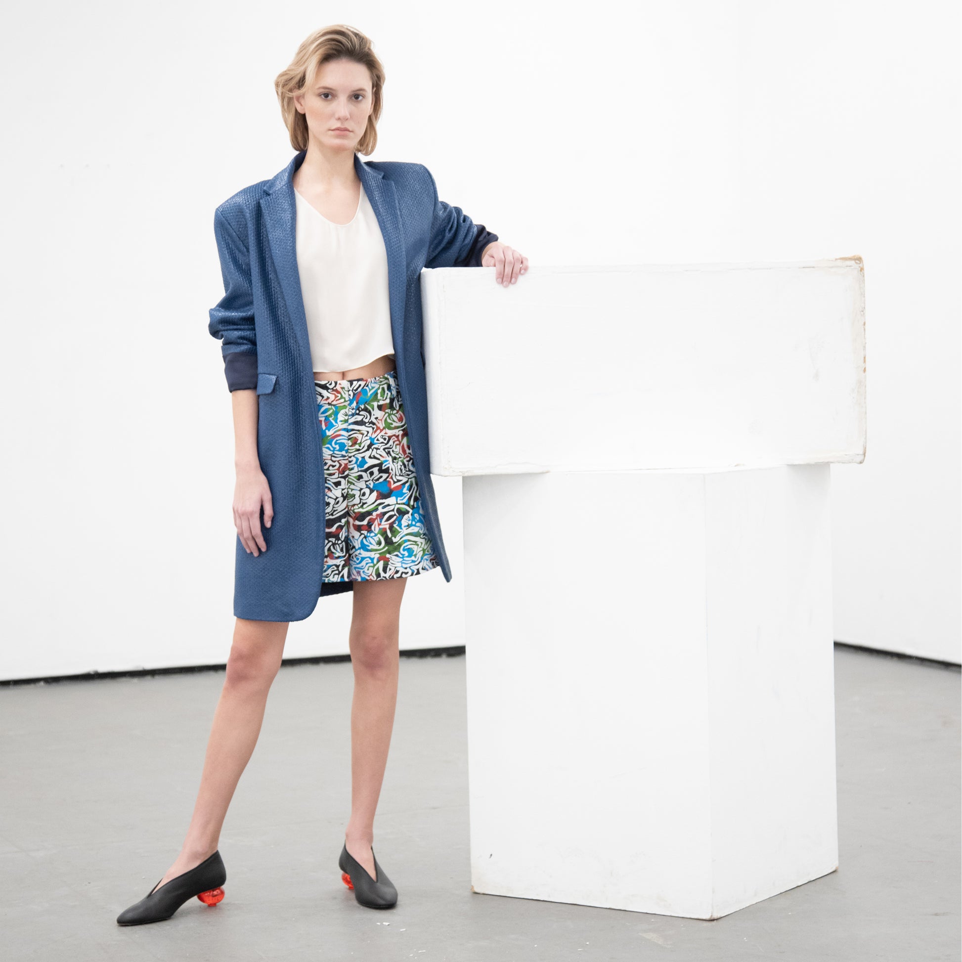 Woman wearing an open style blue blazer cut in a long boyfriend style look over a white shirt and floral shorts'