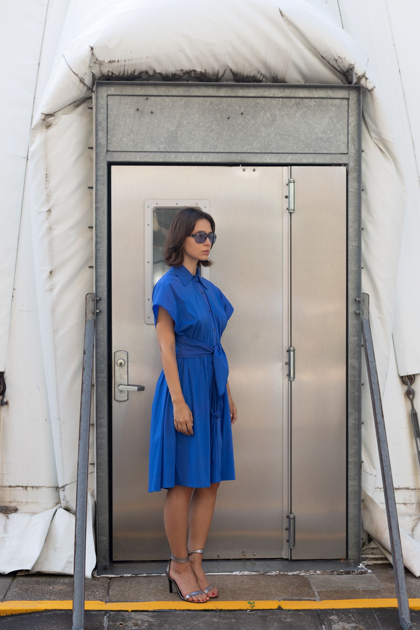 Woman wearing a cupro dress in cobalt blue with button detailing and adjustable waist styled as belt