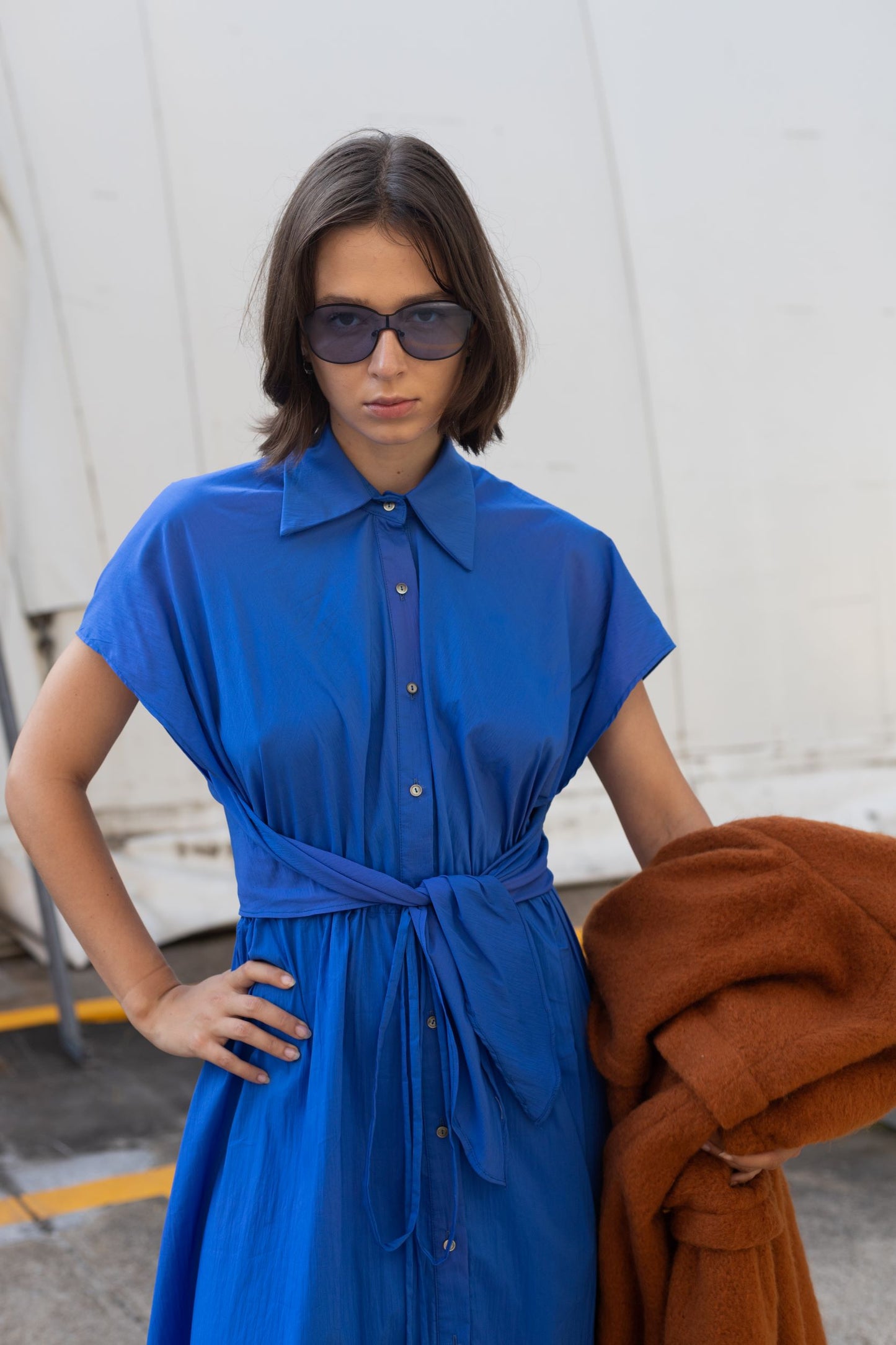 Woman wearing a cobalt blue cupro dress with button detailing and adjustable waist styled as belt