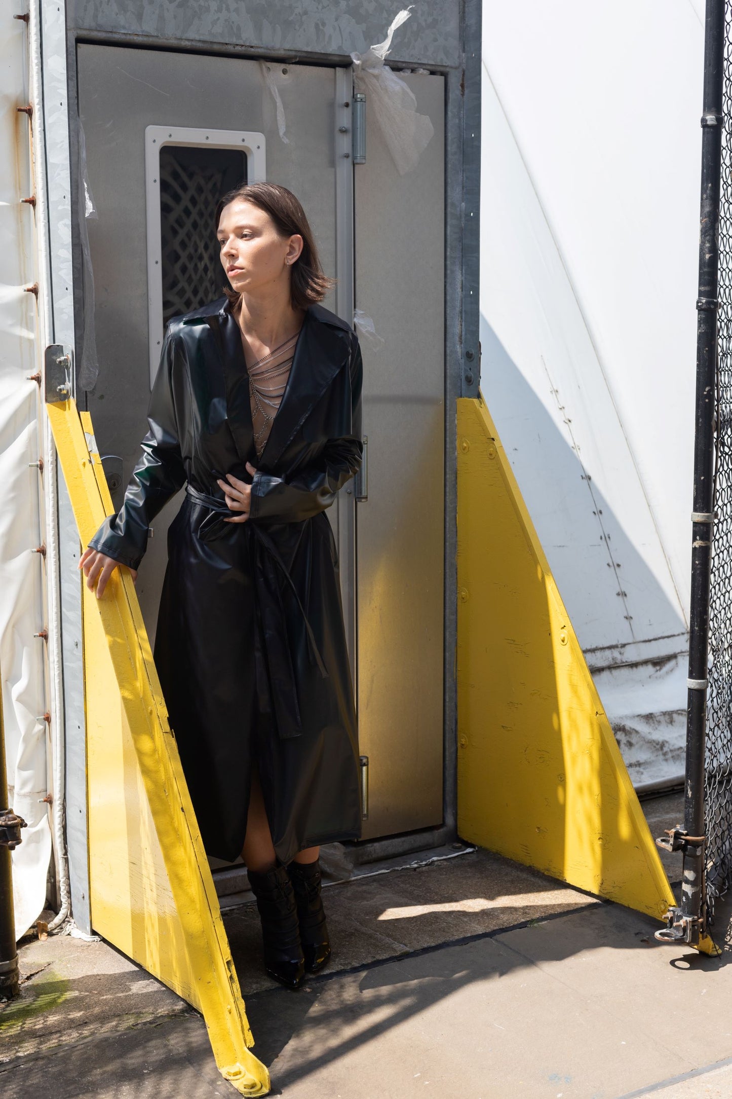 Woman wearing black transitional lambskin trench coat with belt and back metal chain embroidery with jewelry 