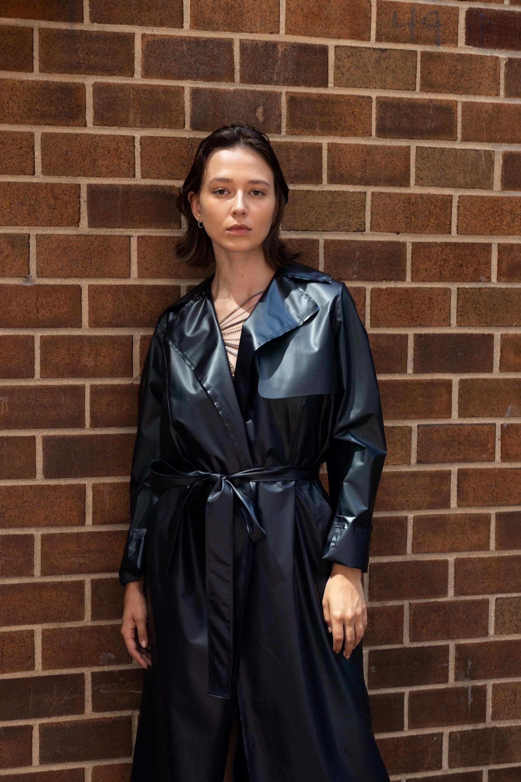 Woman wearing black transitional lambskin trench coat with belt and metal chain embroidery