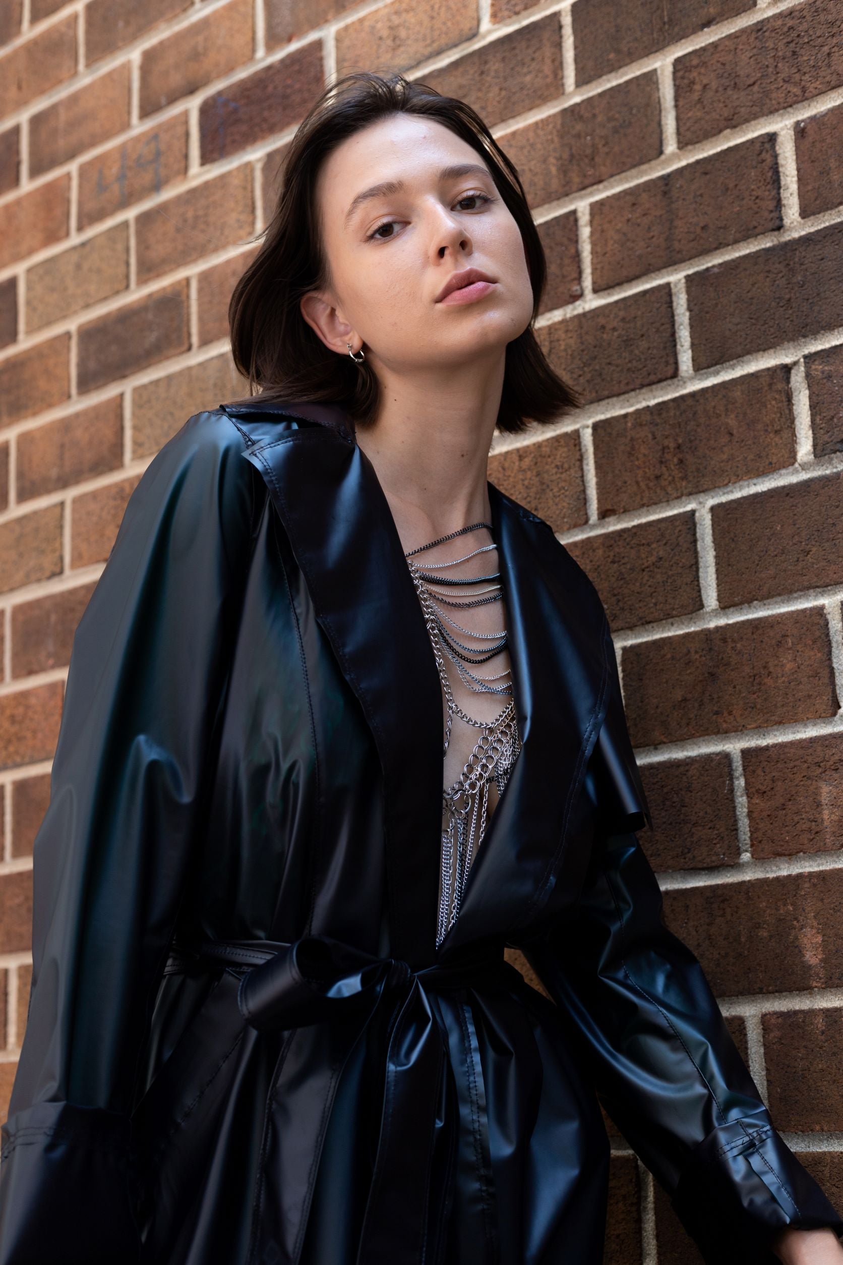 Woman posing with black transitional lambskin trench coat with belt and metal chain embroidery and metal jewelry 